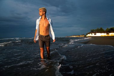 Yaz tatilinde tropik plajda dinlenen şık bir adam. Dertsiz, bronzlaşmış, denizde rahatlayan adamın portresi. Gülümseyen genç adam esintiden ve bakışlardan zevk alıyor..