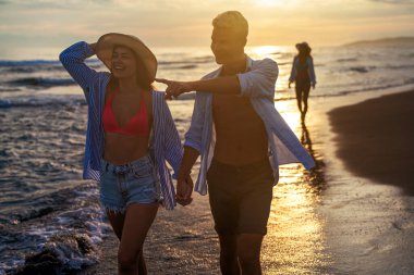 Kumsalda birlikte yürüyen tatilci çift birbirine sarılıyor. Mutlu ırklar arası genç çift yaz tatilinde balayının tadını çıkarıyor.