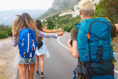 Neşeli ırklar arası arkadaşlar yol kenarında pankartlarla duruyorlar, otostop çekiyorlar, yaz tatilinde arabayı durduruyorlar. Turizm, birlikte seyahat, özgürlük ve arkadaşlık kavramı