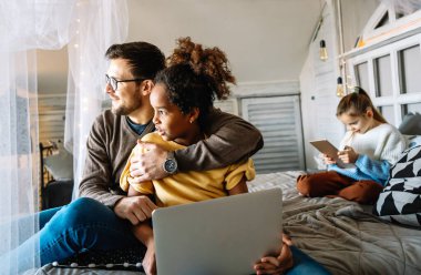 Bekar baba, evdeki dijital tabletle oturma odasındaki yatakta etnik çeşitlilikteki çocuğuyla oynuyor.