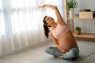 Huzurlu bir eyalette sakin bir hamile kadın yatak odasında doğum öncesi yoga yapıyor. Hamilelik, sağlıklı yaşam tarzı, spor kadını konsepti.