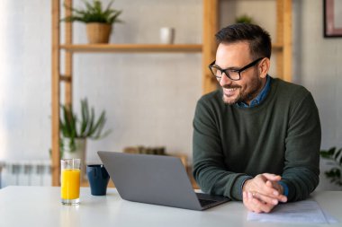Tatmin olmuş yakışıklı adam dizüstü bilgisayarda yazıyor, internetten e-posta yazıyor, uzaktan çalışıyor ya da evde bilgisayar başında çalışıyor.