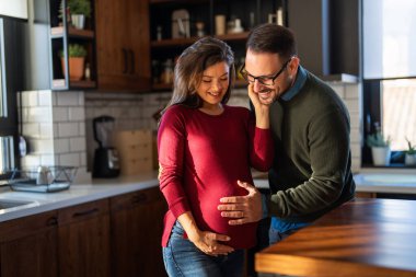 Kocasının birlikte zaman geçirirken hamile eşlerinin karnını sevgiyle kucakladığı şefkatli bir an. Hamilelik, ilişki hedefleri, mutluluk, yeni aile kavramı