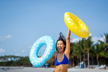 Nihai yaz titreşimleri. Genç bir kadın güneşin sıcaklığından zevk alır, şişme yüzükler tutar ve plaj hayatının keyfini çıkartır.