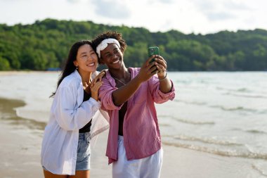 Tropikal bir plajda selfie çeken, tatilin tadını çıkaran, sosyal medya içeriği yaratan ve yaz güneşi altında dijital göçebe yaşam tarzı olan mutlu çiftler.