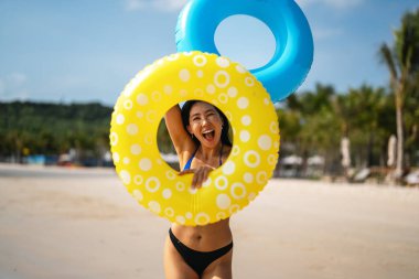 Özgür hissediyorum. Neşeli genç Asyalı bir kadın renkli şişme yüzüklerle ellerini kaldırarak mükemmel bir plaj tatilinin özgürlüğünü kutluyor.