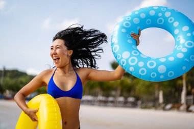 Cennette mutluluk. Gülümseyen genç bir kadın, tropikal kaçışının her anının tadını çıkarıyor. Plajda renkli şişirilebilir yüzüklerle oynuyor.