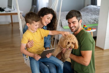 Çocuklu mutlu bir aile tablet bilgisayar kullanarak eğleniyor, ebeveynler ve çocuklar gülüyor evde bilgisayarla komik internet videoları izleyip, online arama yapıyorlar.