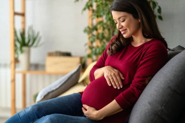 Mutlu hamile anne yatakta oturuyor, tekmelerini hissediyor, koca göbeğini okşuyor, gülümsüyor. Hamile kadın tokuşturuyor, doğmamış bebekle konuşuyor. Annelik, hamilelik kavramı