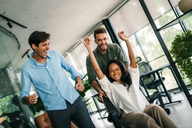 Yaratıcı modern ofisteki aşırı neşeli genç çalışanların portresi. Gülümseyen çok ırklı meslektaşlar, ortak iş başarısını veya görevde kazandığı zaferi kutluyor.