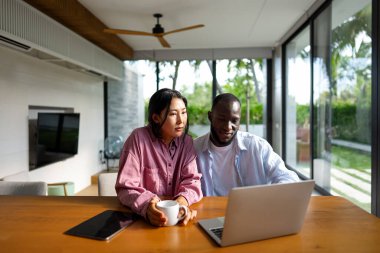 Genç ve çok ırklı çift evde bilgisayar ve dijital cihaz kullanırken eğleniyor. İnsanlar, teknoloji, online yaşam tarzı konsepti