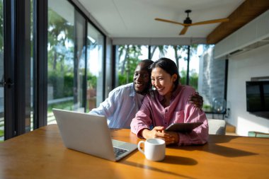 Genç ve çok ırklı çift evde bilgisayar ve dijital cihaz kullanırken eğleniyor. İnsanlar, teknoloji, online yaşam tarzı konsepti