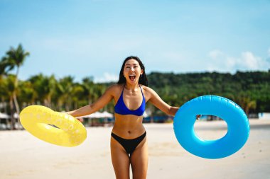 Mutlu genç bir kadın, eğlenceli bir plaj gününün tadını çıkarıyor, okyanus dalgalarında yüzüyor, güneşli gökyüzünün altında gülümsüyor, özgür ve tasasız bir tropikal tatilde.