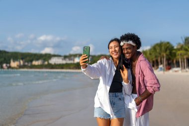 Tropikal bir plajda selfie çeken, tatilin tadını çıkaran, sosyal medya içeriği yaratan ve yaz güneşi altında dijital göçebe yaşam tarzı olan mutlu çiftler.