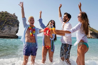 Genç yetişkinler, kumsalda parti yapan arkadaşlar soğuk içecekler ve büyük gülümsemelerle. Deniz kenarında kaygısız bir yaz kutlaması için mükemmel bir sahne.