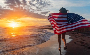 Güzel vatansever, hayat dolu genç bir kadın. Amerikan bayrağı uzanmış ellerinde. Yaz günbatımında ayakta duruyor.