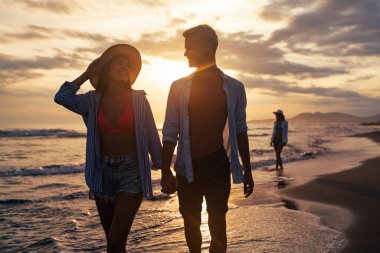 Kumsalda yürüyen bir çift. Genç mutlu ırklar arası çift kumsalda yürüyor gülümsüyor, yaz tatilinin tadını çıkarıyor, balayına çıkıyor.