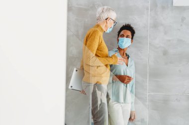 Modern ofiste maske takan iş kadınları, laptopla takım çalışması, salgın sırasında profesyonel iletişim ve işyeri güvenliği