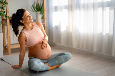 Rahatlamış hamile bir kadın evde bacak bacak bacak üstüne atmış bir şekilde otururken nefes egzersizleri yapıyor.