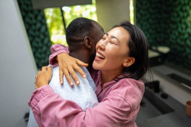 Heyecanlı çocuksuz, etnik çeşitliliğe sahip, modern oturma odasında kucaklaşan ve gülen, sakin bir yaşam tarzı olan çift.