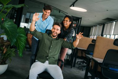 Yaratıcı modern ofisteki aşırı neşeli genç çalışanların portresi. Gülümseyen çok ırklı meslektaşlar, ortak iş başarısını veya görevde kazandığı zaferi kutluyor.