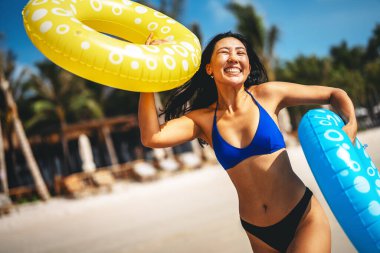 Mutlu genç bir kadın, eğlenceli bir plaj gününün tadını çıkarıyor, okyanus dalgalarında yüzüyor, güneşli gökyüzünün altında gülümsüyor, özgür ve tasasız bir tropikal tatilde.