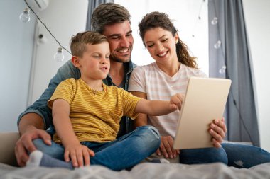 Çocuklu mutlu bir aile tablet bilgisayar kullanarak eğleniyor, ebeveynler ve çocuklar gülüyor dijital cihazla evde dinleniyorlar, komik internet videoları izliyorlar, online arama yapıyorlar.