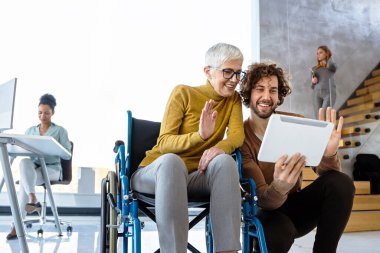 Nesiller arası profesyonellerden oluşan bir grup bir iş toplantısı yapıyor. Tekerlekli sandalye kullanan ve modern bir ofiste takım çalışmasını tasvir eden birini içeriyor.