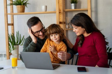 Çocuklu mutlu bir aile birlikte dizüstü bilgisayar kullanarak eğleniyor, ebeveynler ve çocuklar evde gülüyor bilgisayarla komik bir internet videosu izliyor, online arama yapıyor.