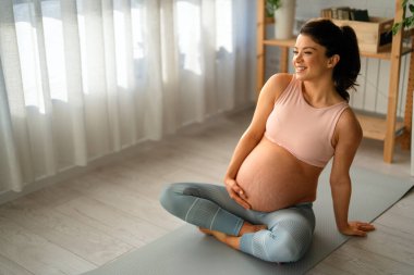 Evde çalışan hamile bir kadının portresi. Hamile kadın evde yoga yapıyor. Hamilelik yogası ve fitness.
