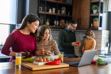 Mutlu ebeveynler mutfak tezgahında çocuklarıyla yemek tarifi hakkında konuşuyorlar ve birlikte hafta sonunun tadını çıkarıyorlar.