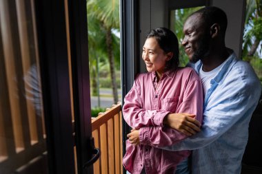 Heyecanlı çocuksuz, etnik çeşitliliğe sahip, modern oturma odasında kucaklaşan ve gülen, sakin bir yaşam tarzı olan çift.