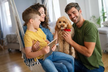 Çocuklu mutlu bir aile tablet bilgisayar kullanarak eğleniyor, ebeveynler ve çocuklar gülüyor dijital cihazla evde dinleniyorlar, komik internet videoları izliyorlar, online arama yapıyorlar.