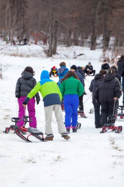 Bakuriani, Georgia 'daki kış parkındaki karlı tepede kızakla tırmanan insanlar.