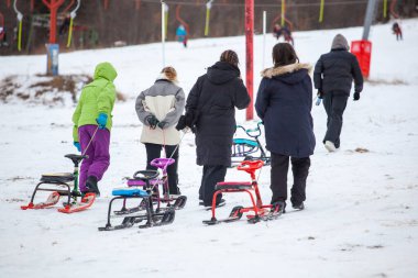Bakuriani, Georgia 'daki kış parkındaki karlı tepede kızakla tırmanan insanlar.