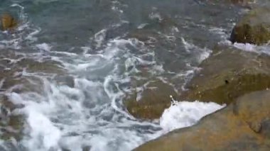 Deniz suyu sahilde taş yıkıyor. Dalgalar kaya uçurumunu kırıyor. Doğa
