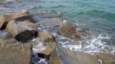 Deniz suyu sahilde taş yıkıyor. Dalgalar kaya uçurumunu kırıyor. Doğa