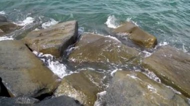 Deniz suyu sahilde taş yıkıyor. Dalgalar kayalıkları ağır çekimde kırıyor