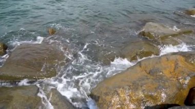 Deniz suyu sahilde taş yıkıyor. Dalgalar kayalıkları ağır çekimde kırıyor