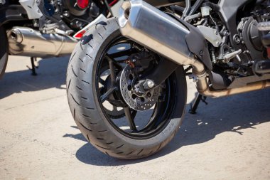 Asfalt üzerinde egzoz borusu olan spor bir motosikletin arka tekerleği. Motor sporu