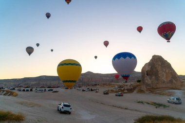 Kapadokya 'da güneş doğarken kayalık arazide uçan sıcak hava balonu. Seyahat