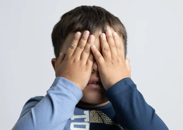 Bust of a child with his hands covering his eyes in fright or excitement of surprise with blue attire on a white background