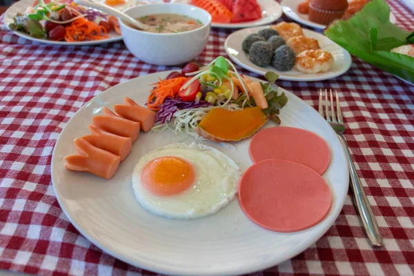 American breakfast with egg, hotdog, and ham on white plate on table