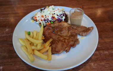 Lokantadaki ahşap masada patates kızartmalı ve salatalı siyah biberli biftek.