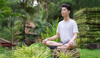 Young man meditating with face raised up to sky and eyes closed at outdoor surrounded by beautiful nature.	
