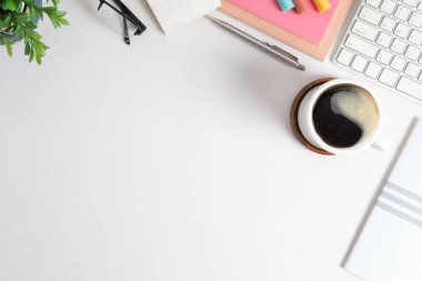 Kadınsı bir iş yeri, kahve fincanı, not defteri, bardaklar ve beyaz masanın üzerinde saksı bitkisi. Metnin için kopyalama alanı olan üst görünüm.