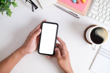 Yukarıdan bakıldığında, beyaz beyaz ekranlı cep telefonu tutan adamın elleri....