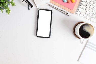Beyaz ekran, kahve fincanı ve beyaz masadaki kırtasiye malzemesi ile üst görünüm akıllı telefon..