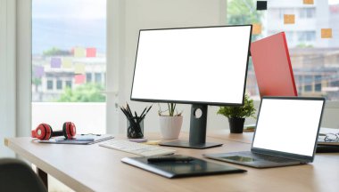 Beyaz boş bilgisayar ekranı, dizüstü bilgisayarı ve ahşap masadaki grafik tableti olan modern işyeri.