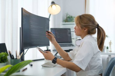 Young woman software developer working with program code on wide displays at modern office.	